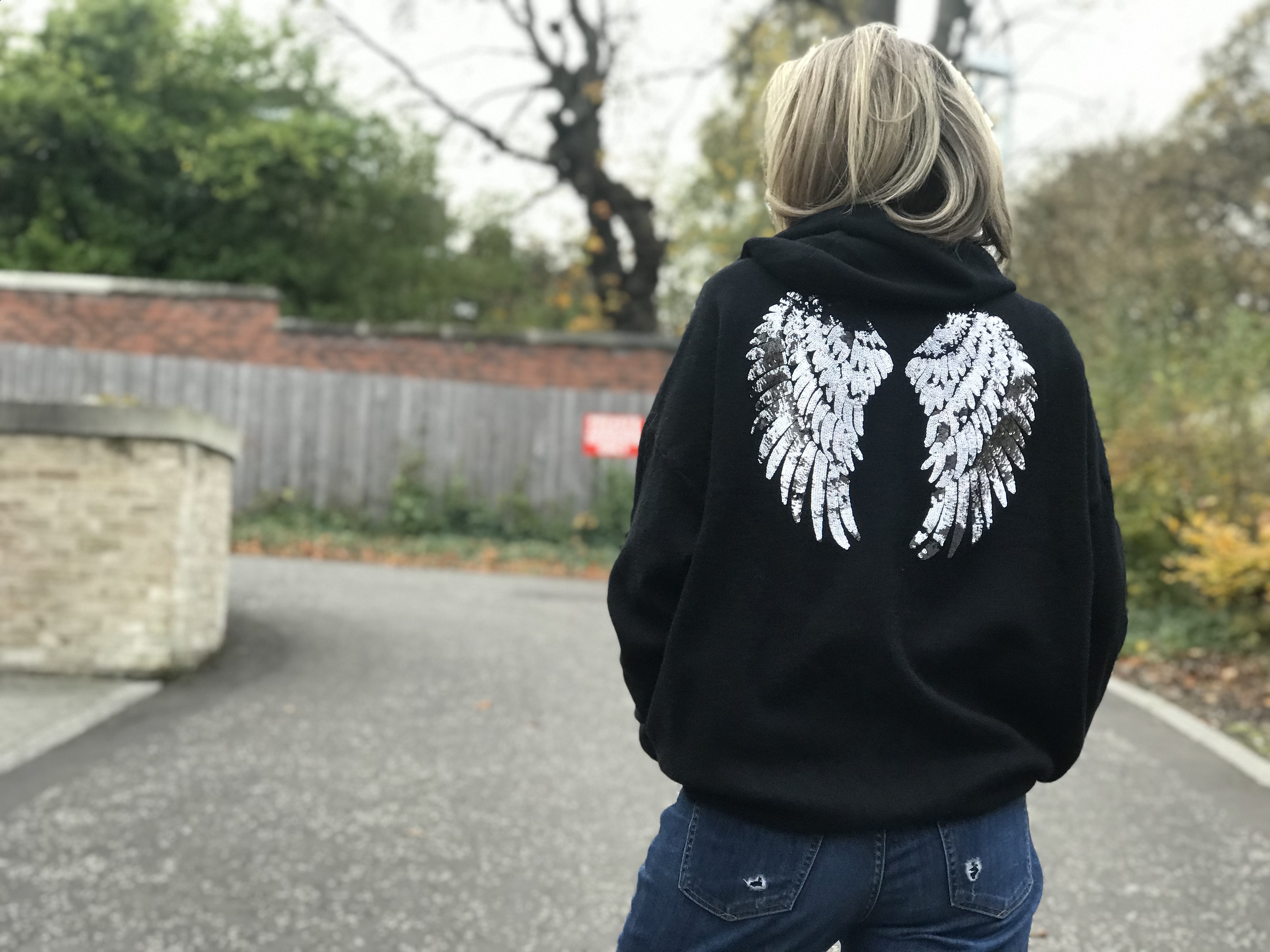 The back of a woman wearing a black hoodie with angel wings