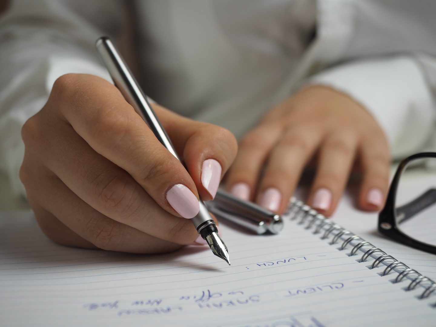 Woman with beautifully manicured healthy nails and pink nail polish, writing with a pen. 