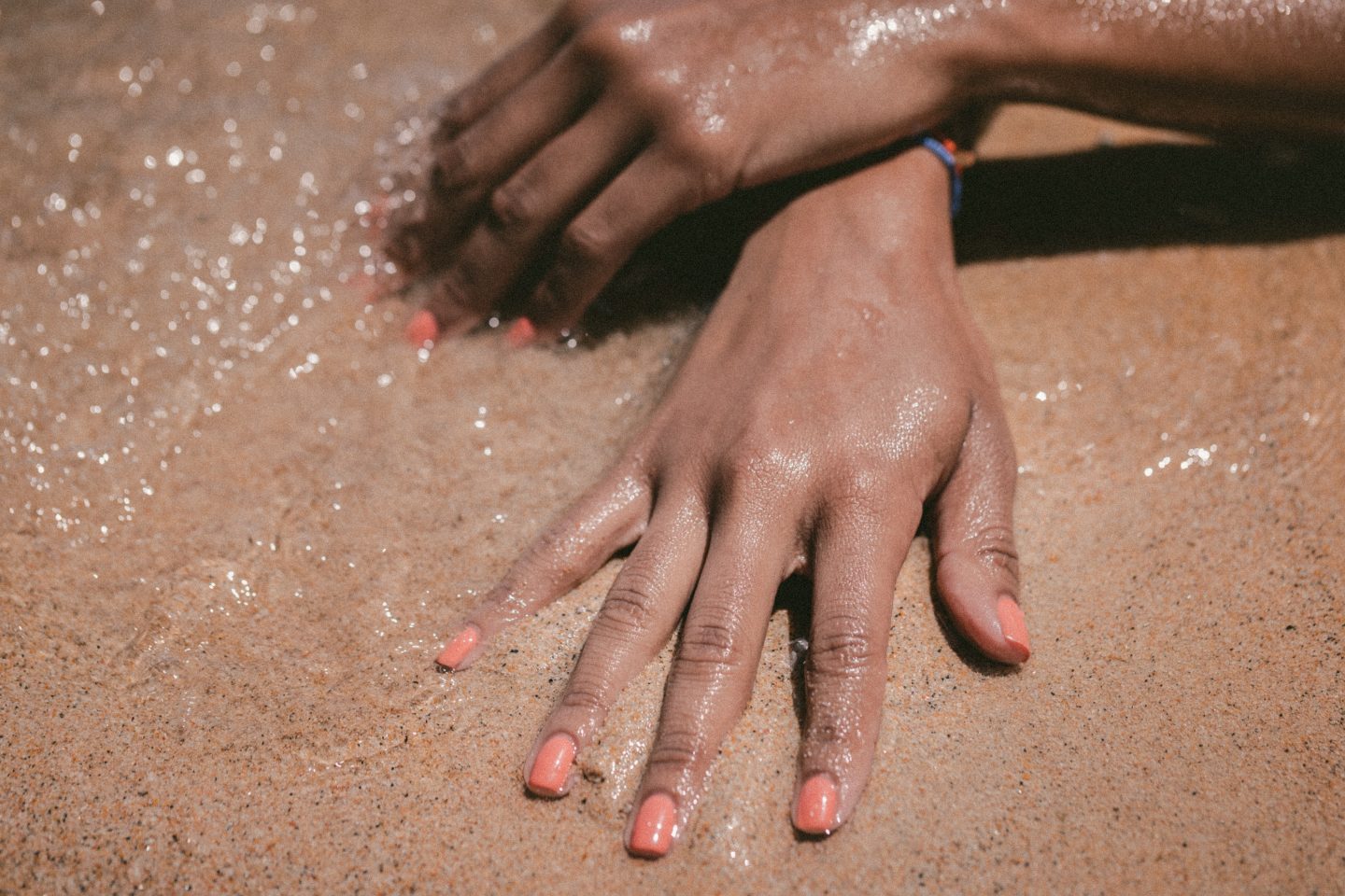 Woman with manicured healthy nails and coral nail polish with hands on wet sand